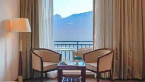 Quarto de hotel com varanda, duas cadeiras, uma mesa e um abajur.