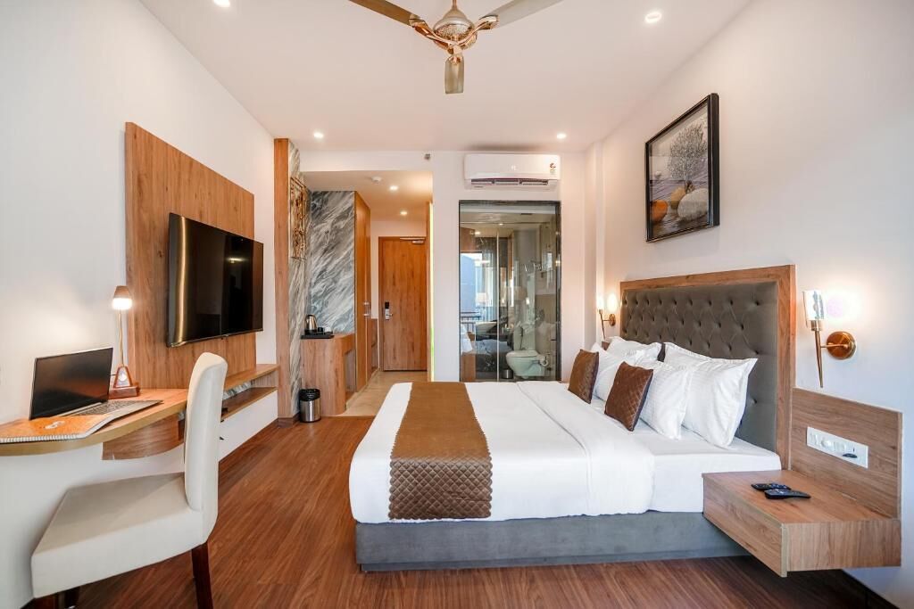 A modern hotel room with a bed, desk, chair, TV, and artwork.