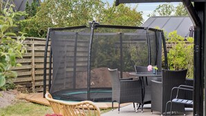 Un área de trampolín cubierta con mobiliario de mimbre cercano y una terraza de madera.