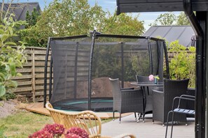 A covered trampoline area with adjacent wicker furniture and a wooden deck. - Charming 70s retreat near beach and peaceful vibe (Odder)