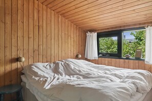 Un dormitorio con paredes de madera, una cama, un ventanal con cortinas y una lámpara fijada a la pared.