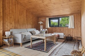 A cozy room with a wooden interior, a sofa, a table, and a window with curtains. - Charming 70s retreat near beach and peaceful vibe (Odder)
