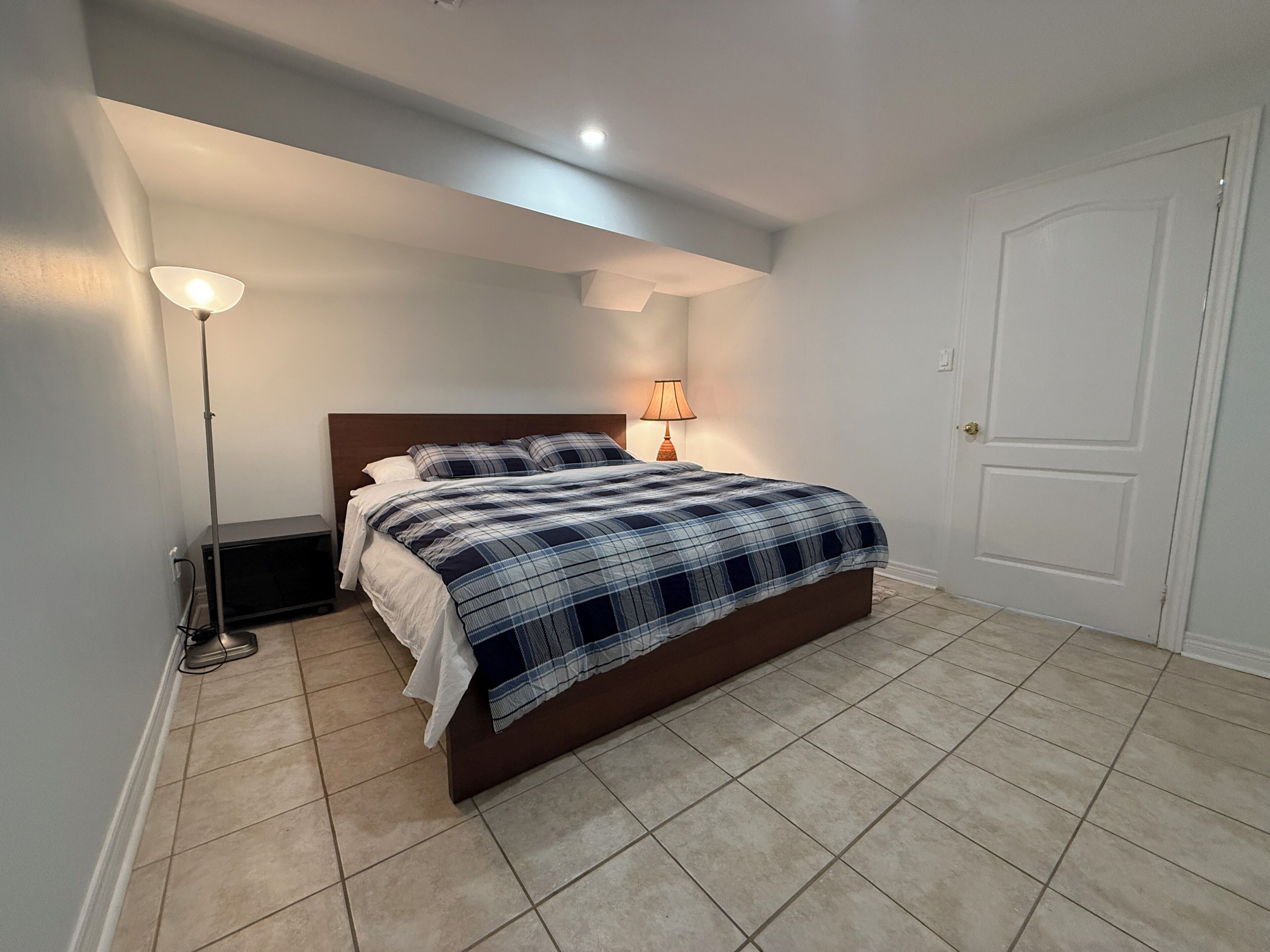Un dormitorio con cama, mesita de noche, lámpara y una puerta.
