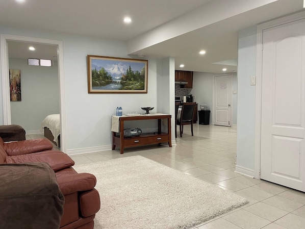 A living room with a brown leather sofa, a white rug, a wooden console table with a radio, and a framed painting of a mountain landscape. - Entire Privatesuite Separate Entrance Free Parking (Richmond Hill)