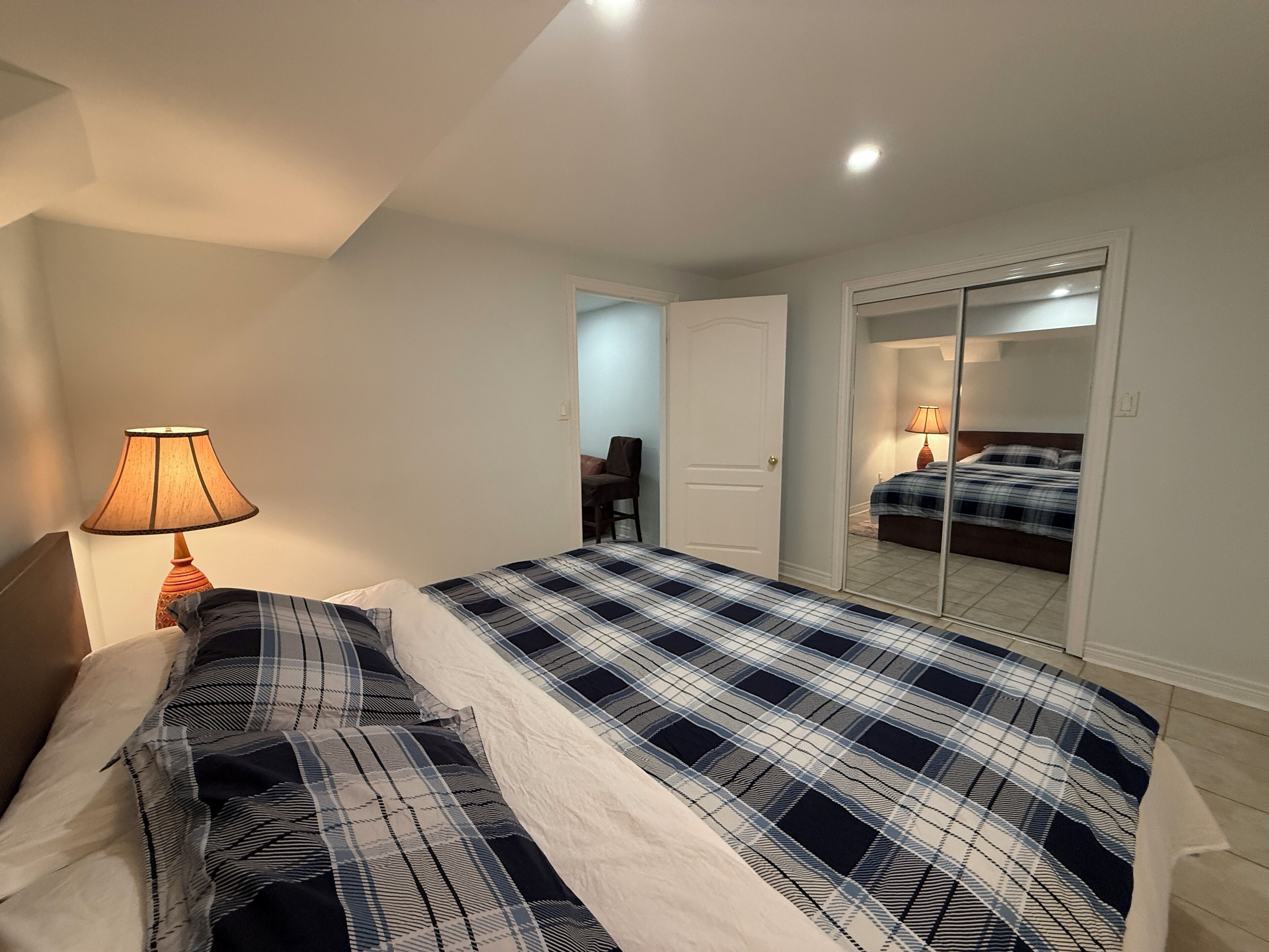 Een slaapkamer met een bed, een lamp, een deur en een spiegel.