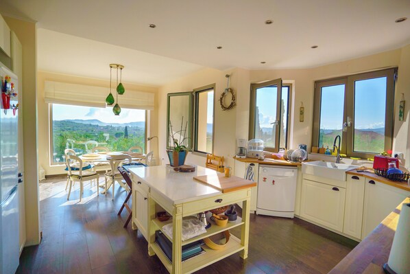 A kitchen with a dining area, large windows, and a view of the outdoors. - Villa Rodi - 3 Bedroom Holiday Home (Zakynthos)