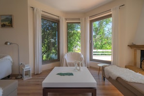 A room with a white table, a chair, a sofa, and large windows with curtains. - Villa Rodi - 3 Bedroom Holiday Home (Zakynthos)
