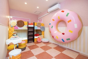 Una sala de juegos infantil con una decoración grande de rosquilla, una litera y una mesita con un pastel.
