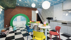 Un espace de jeux pour enfants avec des trottinettes, un sol à carreaux et un coin cuisine équipé d’appareils électroménagers modernes.