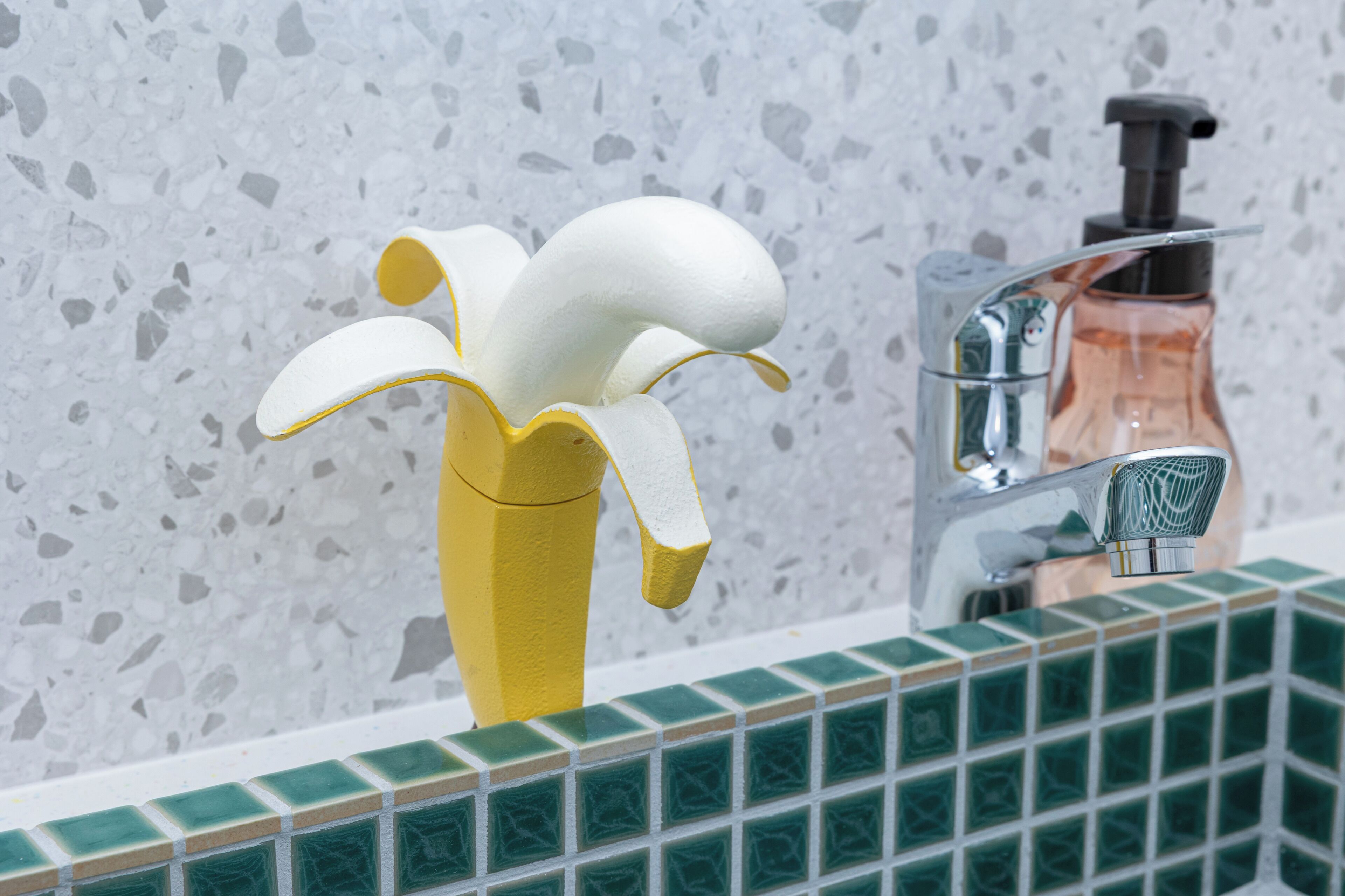 Un baño con un grifo amarillo distintivo, un dispensador de jabón y azulejos verdes.