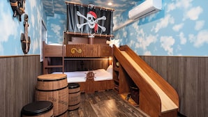 Un lit superposé décoré d’étoiles, une glissoire en bois et des barils étiquetés « CAFÉ DE LA MONTAGNE ELLE ».