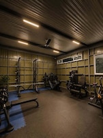 Uma academia com equipamentos de musculação, bicicletas ergométricas e um ventilador de teto.