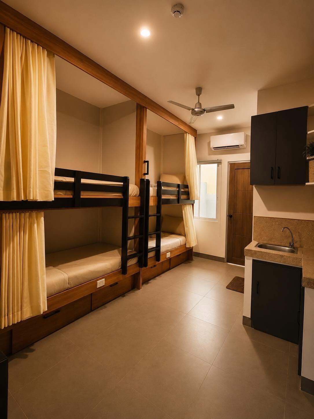 A compact room with bunk beds, a kitchenette, and a ceiling fan.