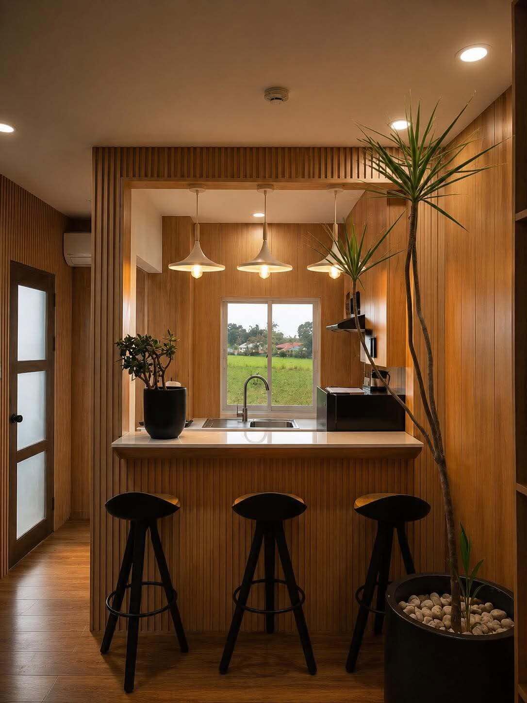 A modern kitchen with wooden paneling, pendant lighting, a large window, and a potted plant.