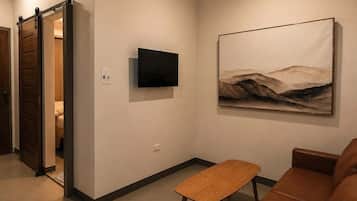 Una sala de estar con un sofá de cuero marrón, una mesa de centro de madera, un televisor de pantalla plana montado y un ventilador de techo.