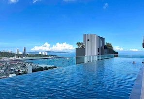 A modern infinity pool with a cityscape and ocean view. - Sea View 2 Bed Room I Best Of Location (Pattaya)