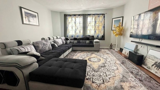 Una sala de estar con un sofá modular, un televisor de pantalla plana grande y una alfombra estampada.