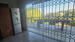 A room with a refrigerator, a wooden door, and a view through a metal gate to an outdoor area. - La Lucia Home With a View (uMhlanga)