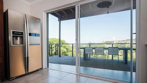 A kitchen with a refrigerator, a water dispenser, and a sliding glass door leading to an outdoor deck with a table and chairs. - La Lucia Home With a View (uMhlanga)