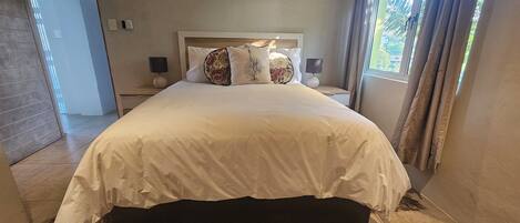 A neatly made bed with a white bedspread, two bedside lamps, and a window with curtains.