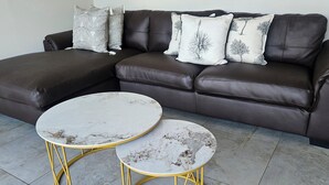 A brown leather sectional sofa with patterned pillows, two marble-topped round tables with gold legs, and grey tiled flooring. - La Lucia Home With a View (uMhlanga)