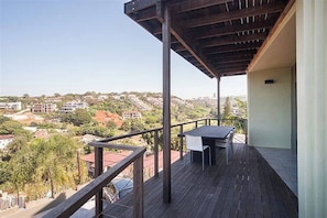 A balcony with a table and chairs, overlooking a residential area with houses and greenery. - La Lucia Home With a View (uMhlanga)