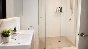 A modern bathroom with a glass-enclosed shower, a white sink, and a marble countertop. - The Sunset Perch | Panoramic River Escape (South Brisbane)