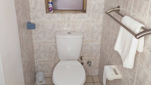 A small bathroom with a toilet, a window, a towel rack, and a cleaning spray.