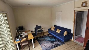 A small living room with a blue sofa, a wooden dining table, and a patterned rug.