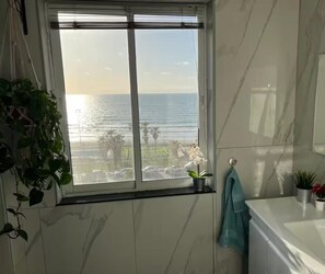A bathroom with a large window, marble walls, a sink, and a towel rack. - Vacation apartment first line view to the sea, fully equipped penthouse (Bat Yam)
