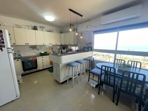 A modern kitchen with white cabinets, a central island, bar stools, and a dining table with chairs. - Vacation apartment first line view to the sea, fully equipped penthouse (Bat Yam)