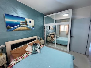 A bedroom with a bed, a nightstand, a dresser, a mirror, and a painting on the wall. - Vacation apartment first line view to the sea, fully equipped penthouse (Bat Yam)