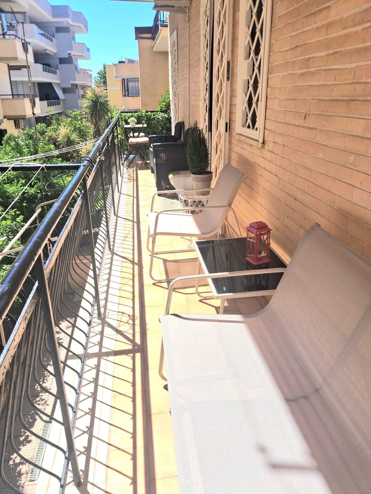 Un balcone con ringhiera in metallo, sedie imbottite bianche, un tavolino e una pianta in vaso.