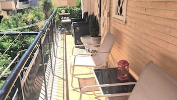 Un balcone con ringhiera in metallo, sedie imbottite bianche, un tavolino e una pianta in vaso.