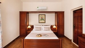Habitació d'hotel amb llit de fusta, dues taules de nit, aire condicionat fixat a la paret i un quadre encimbellat sobre el llit.