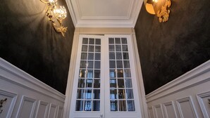 Een statig entree met een dubbele deur, een donker plafond en twee wandlampen.