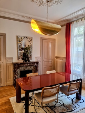 Uma sala de jantar com uma mesa grande, cadeiras, lareira e uma janela com cortinas.