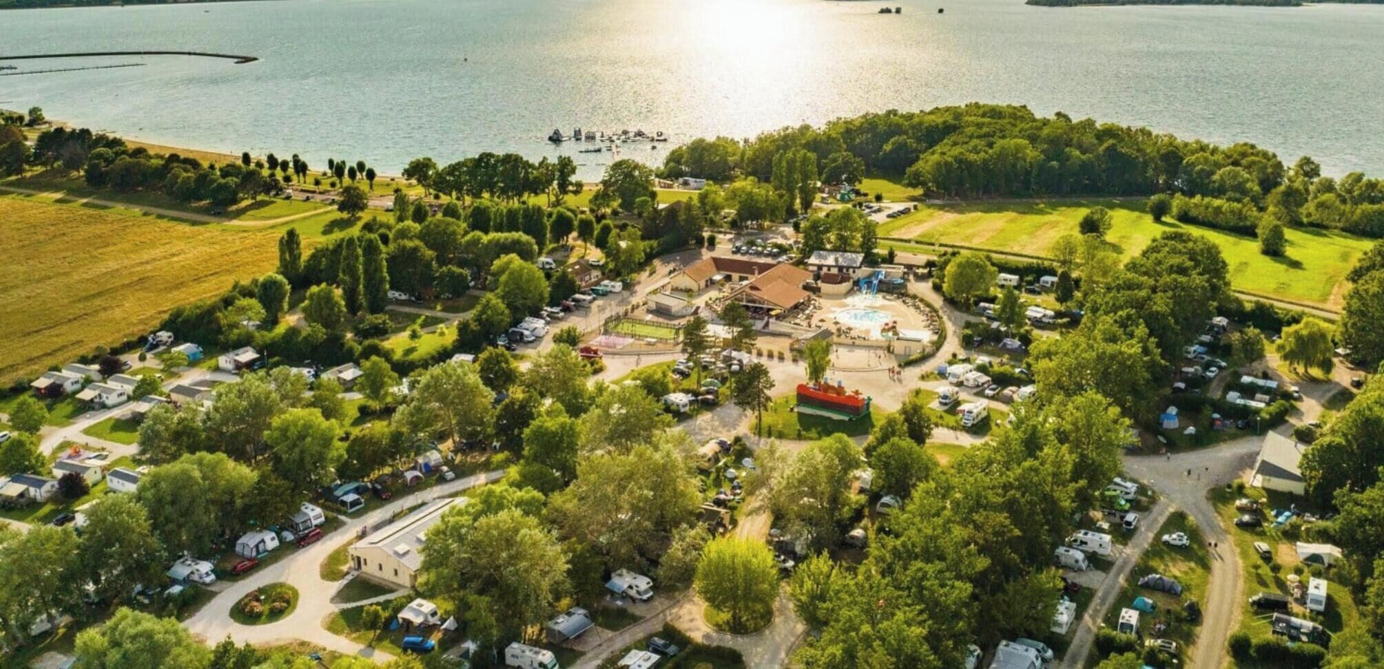 Vue aérienne d’un terrain de camping avec des camping-cars, une piscine et un lac.