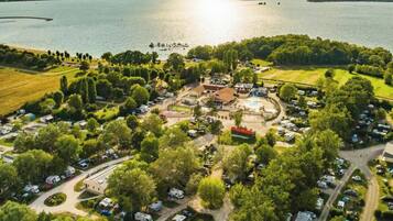 Vue aérienne d’un terrain de camping avec des camping-cars, une piscine et un lac.
