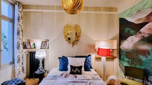 Een slaapkamer met een groot bed, een spiegel in de vorm van een hart, een kroonluchter, een boekenkast, een rode lamp en een schilderij aan de muur.