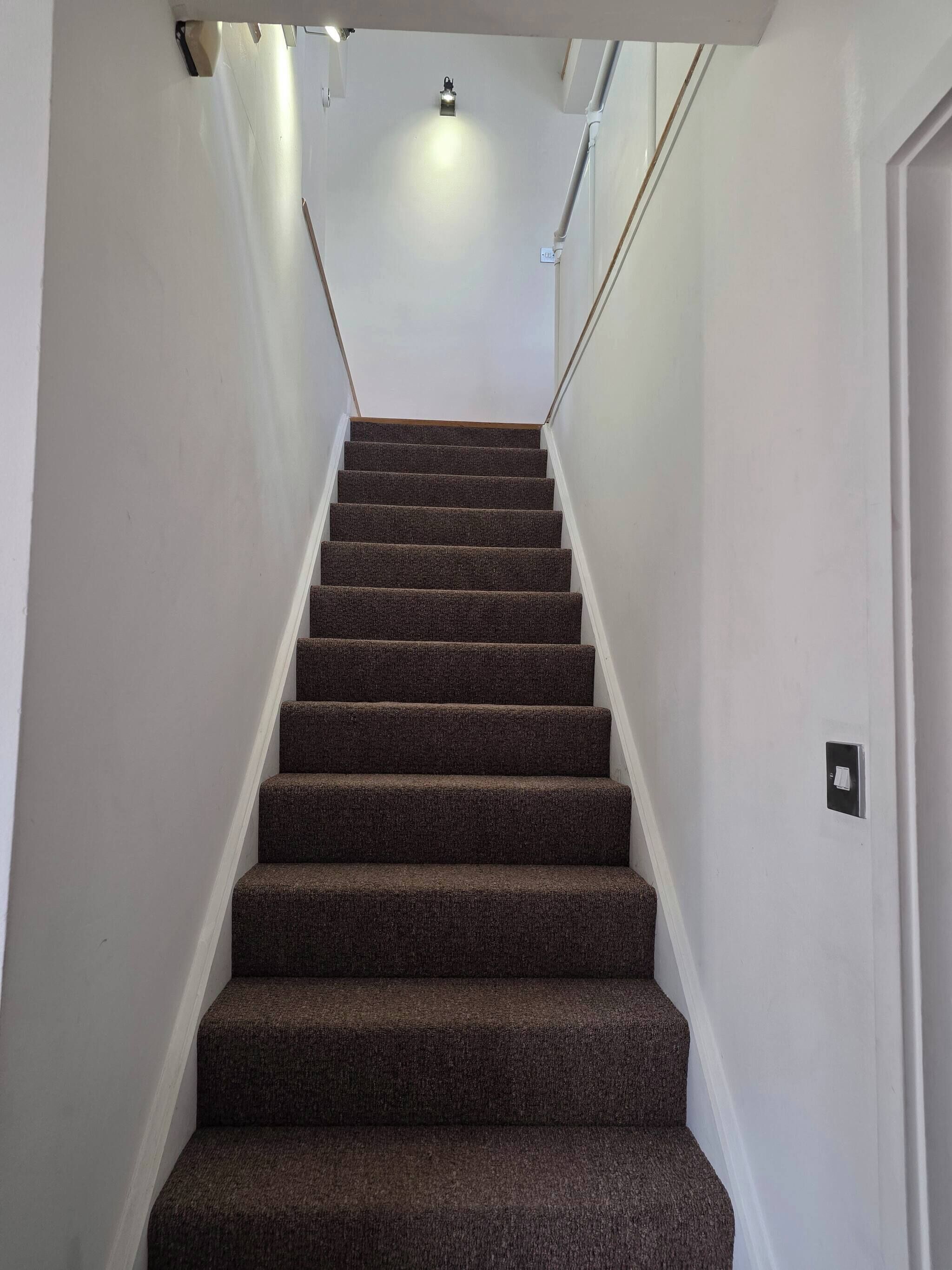 A carpeted staircase with white walls and a light fixture at the top.