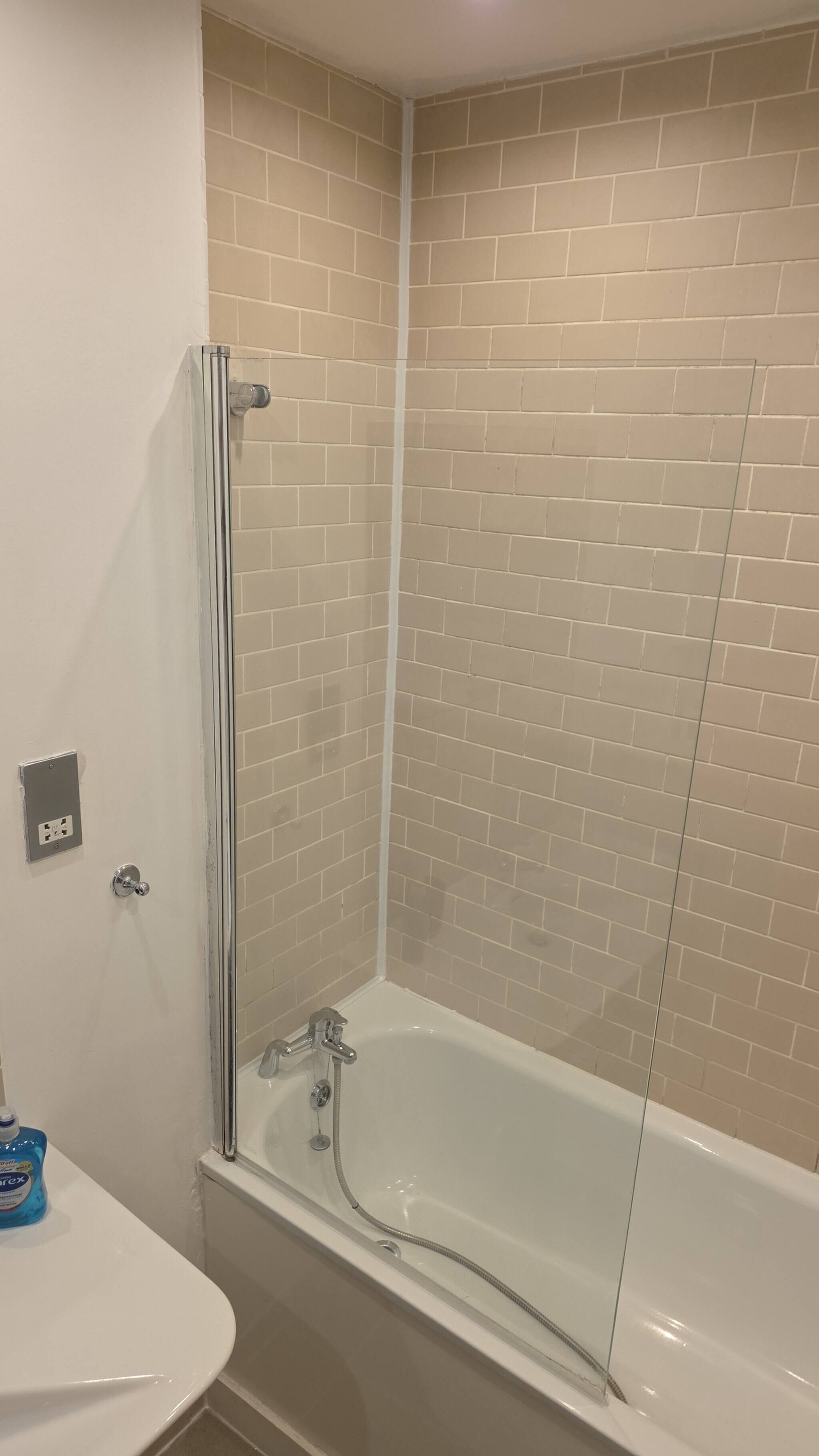 A bathroom with a glass shower enclosure, a white bathtub, and a sink with a bottle of hand soap.
