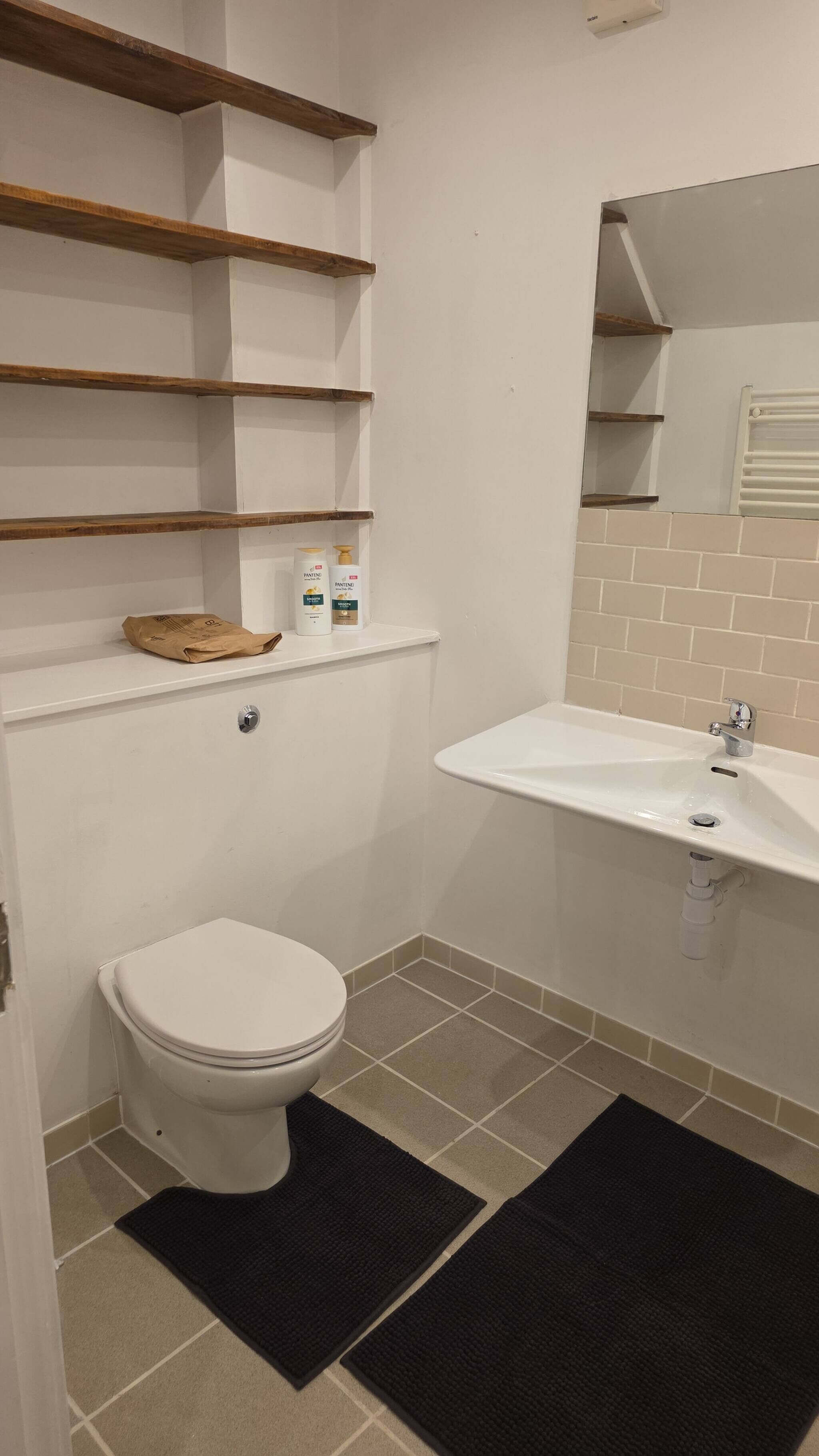 Un bagno con il water, un lavandino e mensole in legno sopra il water.