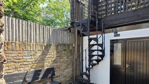 A brick wall, a black metal bench, a spiral staircase, and a black door. - Boutique Dairy Conversion Near Ilford Station (Ilford)