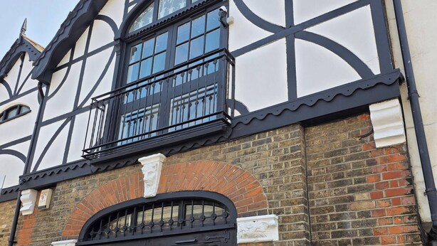 A Tudor-style building with a black and white facade, a large arched window, and a black gate. - Boutique Dairy Conversion Near Ilford Station (Ilford)