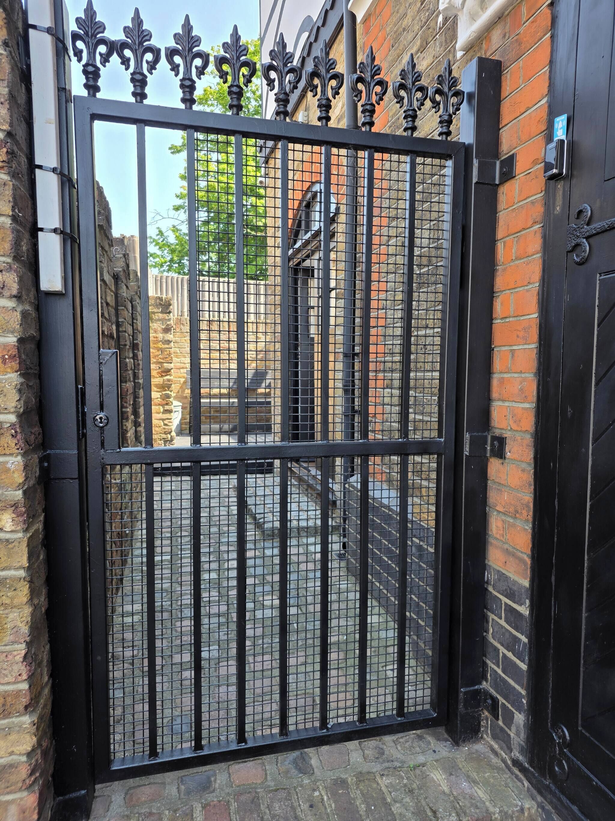 A black metal gate with decorative elements, a brick wall, and a door to the right.