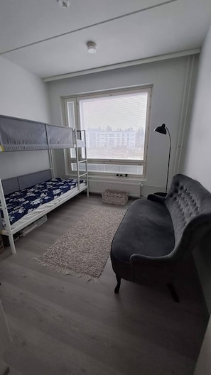 Una habitación pequeña con literas, un sofá, una lámpara y una ventana con persianas.