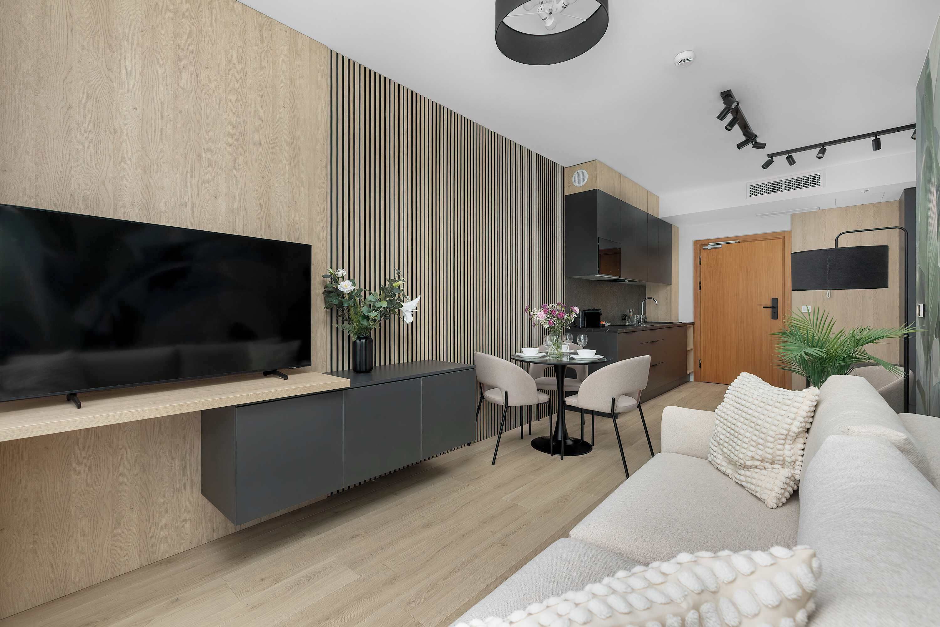 Un salon moderne avec un téléviseur à écran plat, un canapé, un coin repas avec des chaises et une cuisine en arrière-plan.