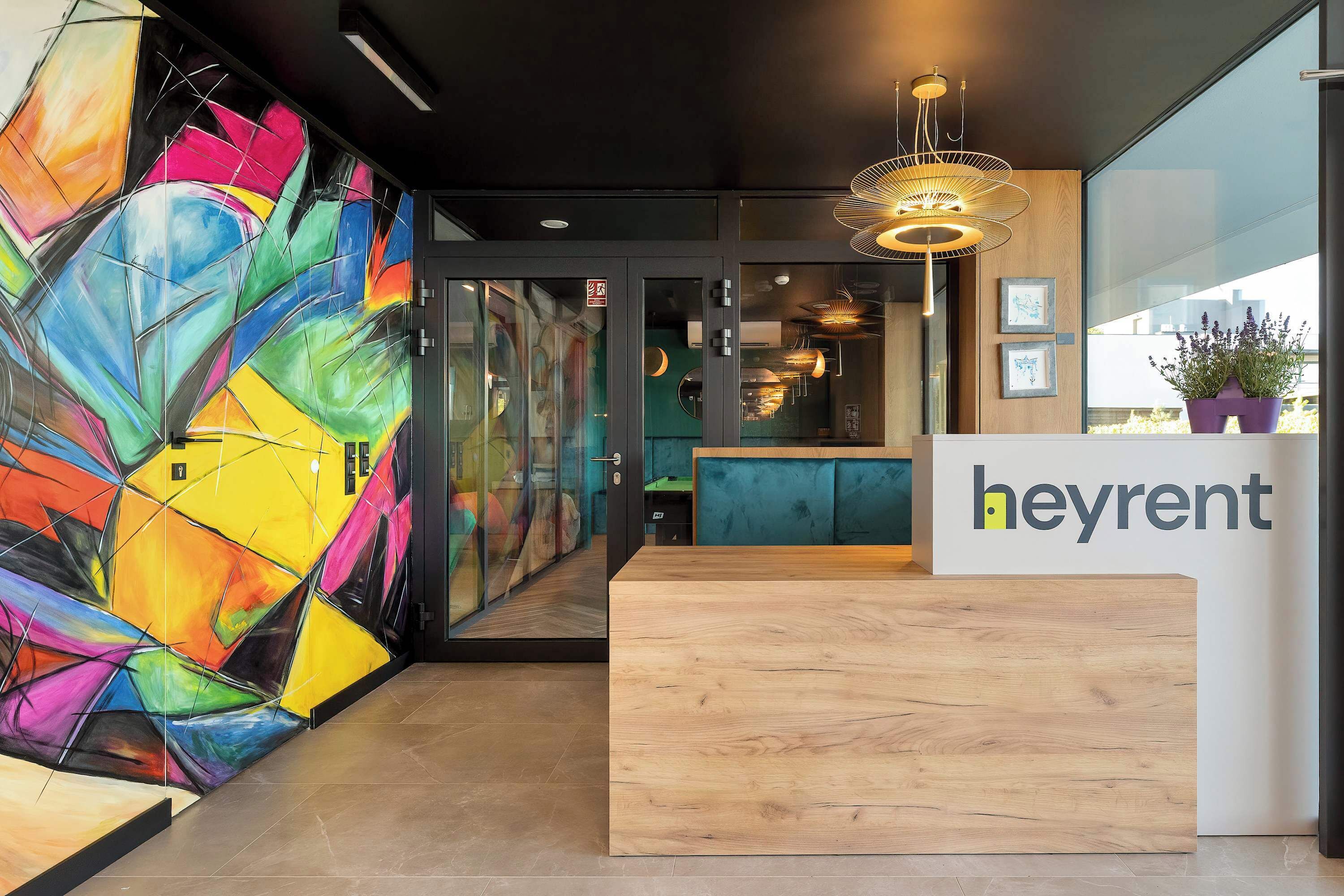 A modern reception desk with a colorful abstract mural, a wooden reception area, and a view of the city through large windows.