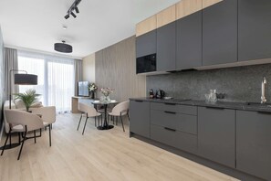 A modern kitchen with dark cabinets, a large island, and a dining area with chairs and a table. - Comfortable Apartment with Air Conditioning and Parking | Close to the Beach (Mielno)